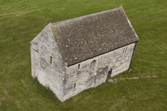 Aerial angled view of Meare Fish House showing stone walls and pitched tiled roof in open field.