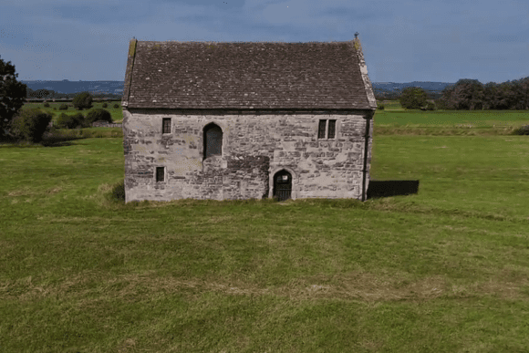 Stone Meare Fish House standing alone in a grassy field with a pitched roof.