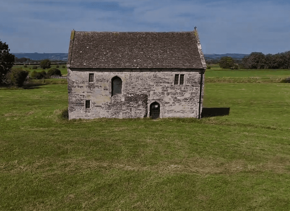 Stone Meare Fish House standing alone in a grassy field with a pitched roof.