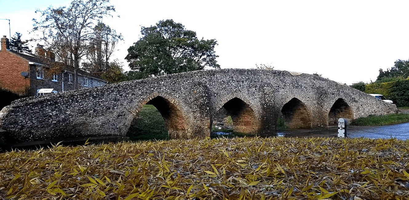Historic stone packhorse bridge with multiple arches over a small stream in Moulton village.