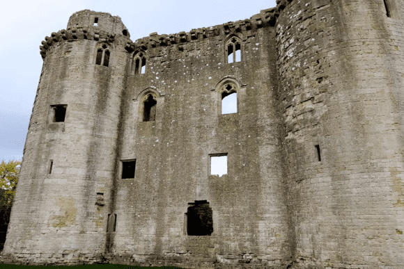 Stone walls and round towers of Nunney Castle ruins with empty window openings and weathered medieval masonry.