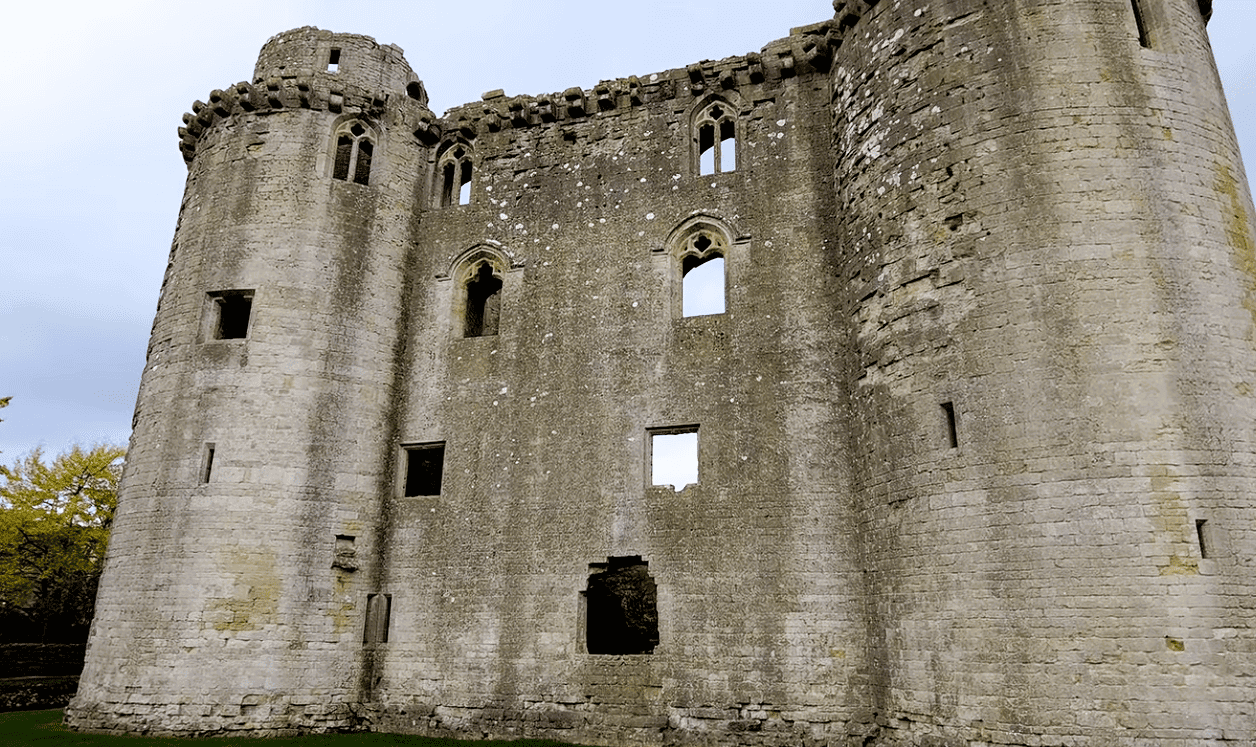 Stone walls and round towers of Nunney Castle ruins with empty window openings and weathered medieval masonry.