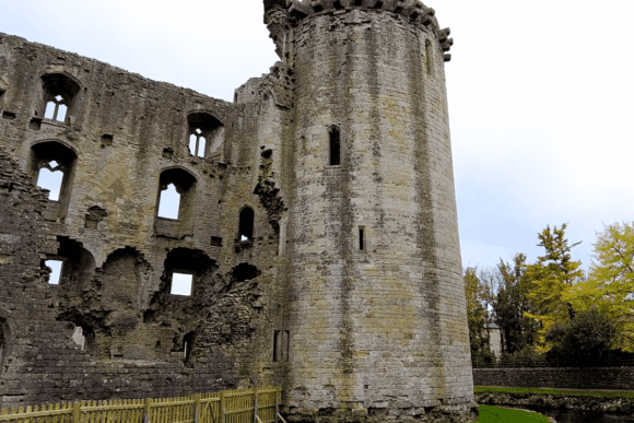 Exterior view of Nunney Castle ruins with a round tower and weathered stone walls featuring empty window openings.
