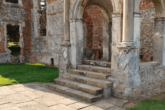 Stone steps leading to an arched entrance within the ruins of Old Gorhambury House, surrounded by red brick and flint walls.