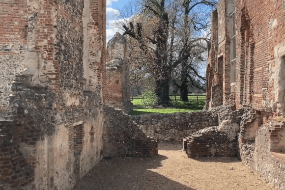 Interior view of Old Gorhambury House ruins with crumbling brick walls, open spaces, and sunlight illuminating the ground.
