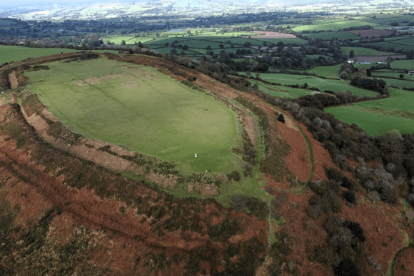 Aerial view of Pilsdon Pen in Dorset, England, showing the Iron Age hillfort earthworks, grassy summit, and surrounding countryside.
