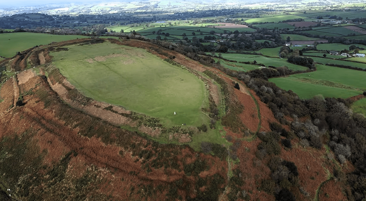 Aerial view of Pilsdon Pen in Dorset, England, showing the Iron Age hillfort earthworks, grassy summit, and surrounding countryside.