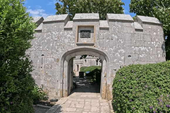Stone entrance gateway of Portland Castle in Dorset, England, featuring an arched doorway, crenellated walls, and surrounding greenery.
