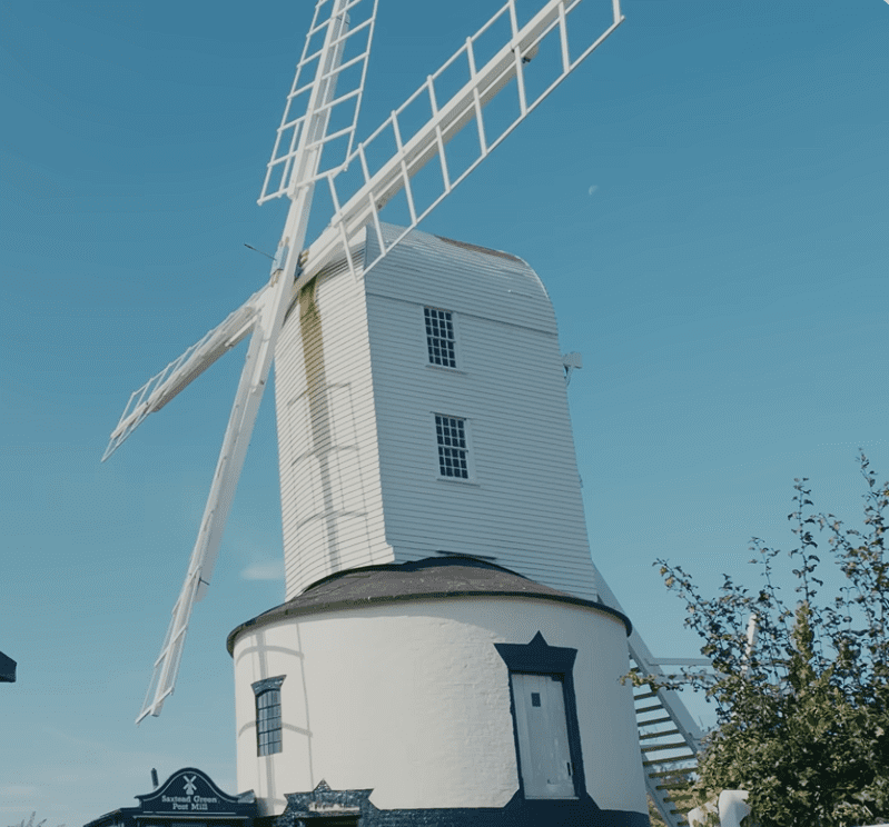 Saxtead Green Post Mill in Suffolk, traditional white wooden windmill with sails against a clear blue sky.