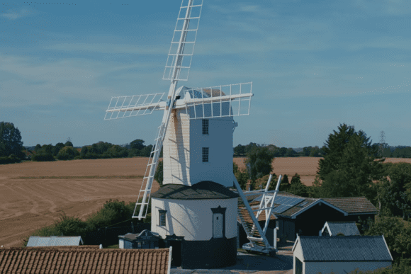 Saxtead Green Post Mill windmill surrounded by countryside fields in Suffolk, England, with traditional sails and rural landscape.