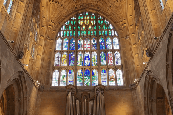Large stained glass window inside Sherborne Abbey above organ pipes, with intricate Gothic stone architecture.