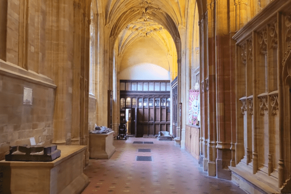Interior aisle of Sherborne Abbey with vaulted ceiling, stone arches, wooden panels, and historic Gothic architecture.