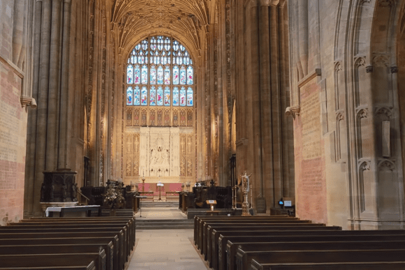 Interior of Sherborne Abbey with wooden pews, vaulted ceiling, ornate altar, and large stained glass window.