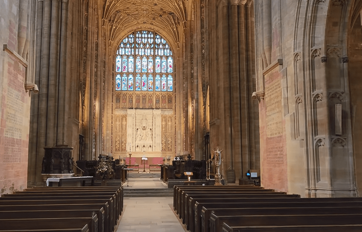 Interior of Sherborne Abbey with wooden pews, vaulted ceiling, ornate altar, and large stained glass window.