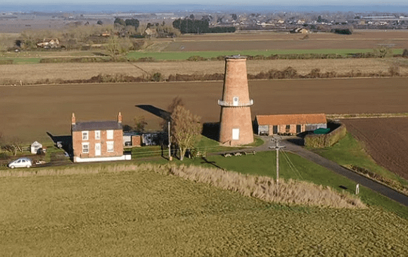 Aerial view of Sibsey Trader Windmill surrounded by farmland, countryside fields, and nearby buildings in Lincolnshire.