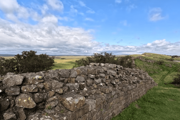 Stone remains of Hadrian’s Wall at Walltown Crags overlooking rolling Northumberland countryside under a dramatic blue sky with scattered clouds.