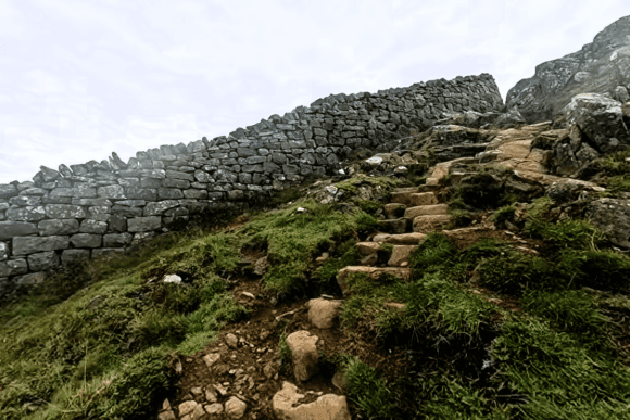 Stone pathway climbing beside Winshields Wall on Hadrian’s Wall, featuring rugged Roman masonry and dramatic countryside terrain in Northumberland, England.