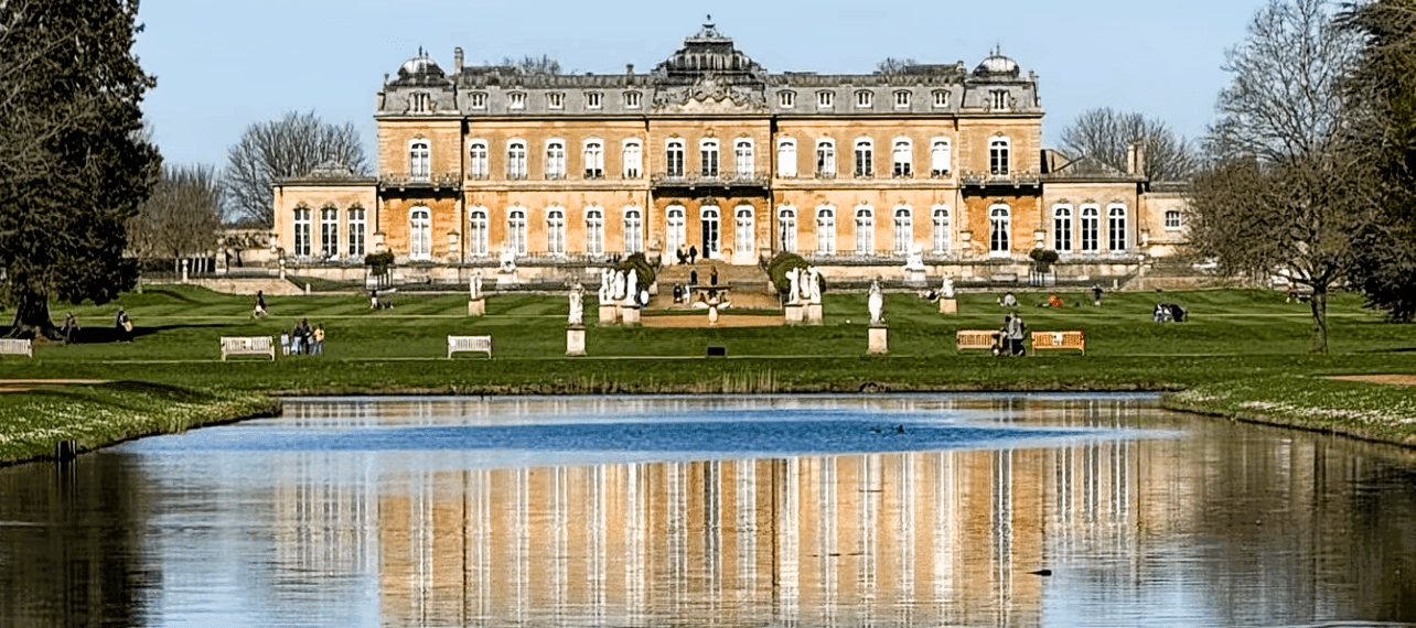 Wrest Park mansion reflected in a tranquil lake, surrounded by formal gardens, statues, and landscaped parkland in Bedfordshire.