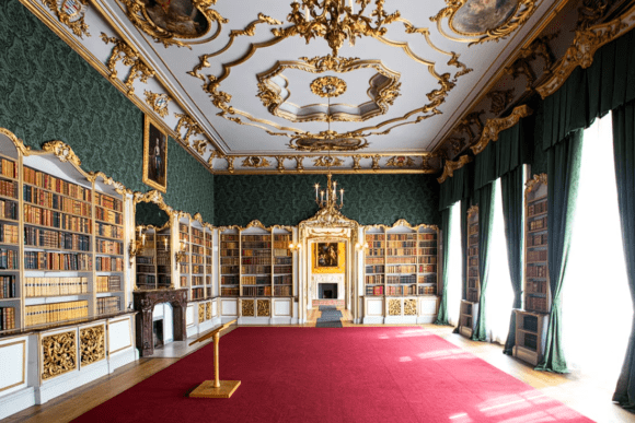 Elegant library room inside Wrest Park featuring ornate gold ceiling decorations, tall bookcases, green drapery, chandeliers, and luxurious Georgian interior design.