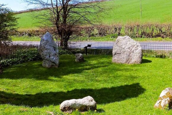 Ancient standing stones at The Nine Stones stone circle surrounded by green countryside and rolling fields in rural England.