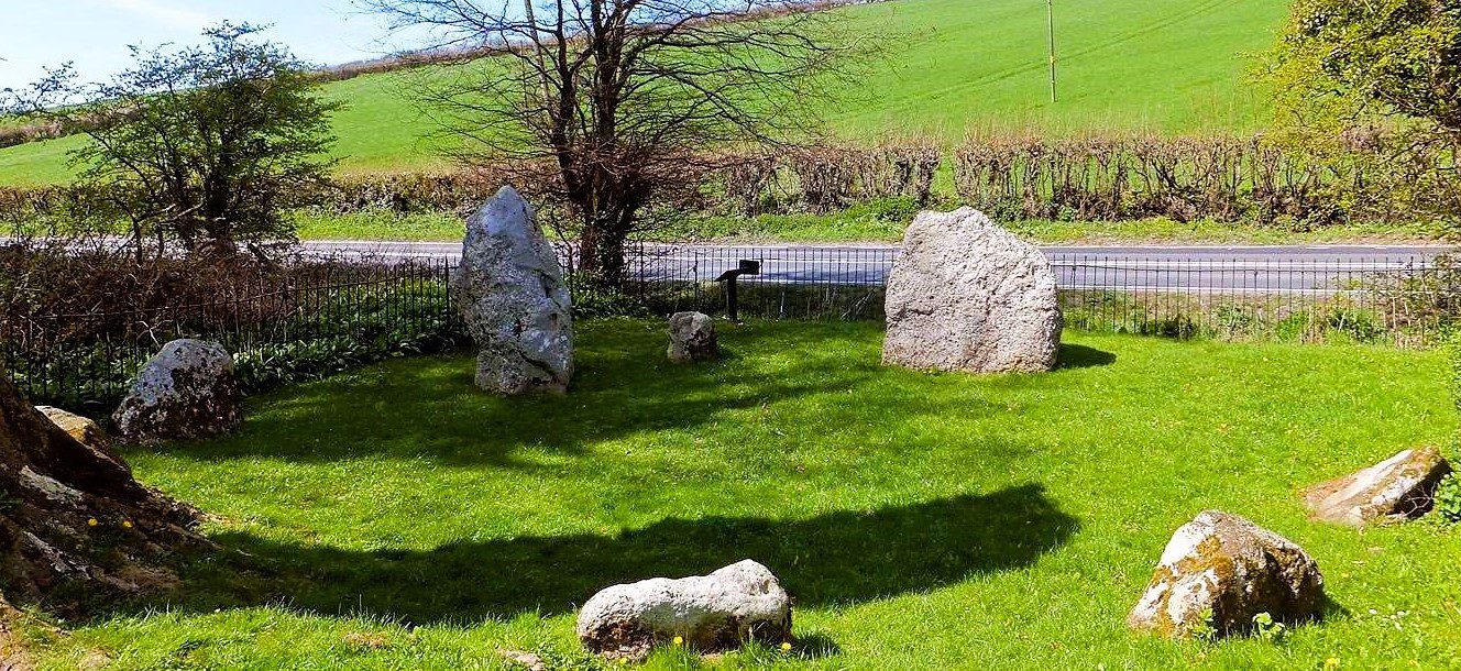 Ancient standing stones at The Nine Stones stone circle surrounded by green countryside and rolling fields in rural England.