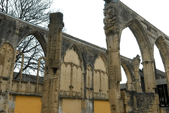 Ruined Gothic stone arches and partial walls of Greyfriars, with pointed arch windows and exposed masonry.