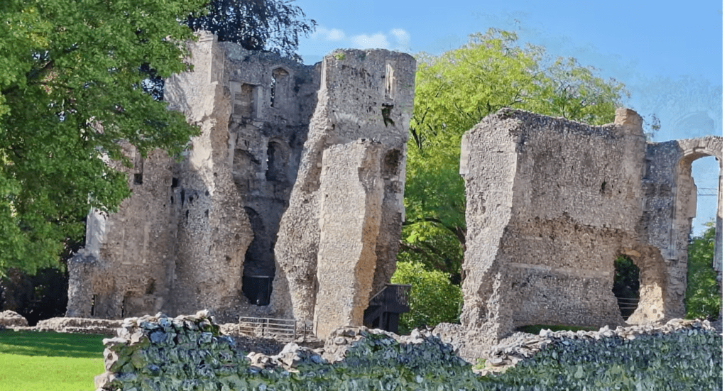 Ruins of Bishop’s Waltham Palace showing stone walls and arched openings among green trees.