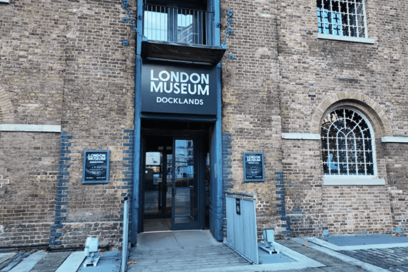 Entrance to the Museum of London Docklands in Canary Wharf, featuring a historic brick warehouse façade, arched windows, and the museum’s main sign above the doorway.