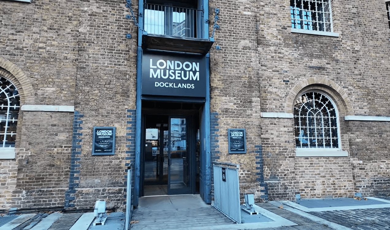 Entrance to the Museum of London Docklands in Canary Wharf, featuring a historic brick warehouse façade, arched windows, and the museum’s main sign above the doorway.
