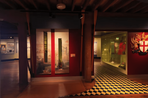 Historic gallery exhibit inside the Museum of London Docklands featuring timber beams, maritime displays, a City of London crest, and interactive heritage exhibits exploring London’s trading and docklands history.